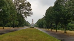 Bäume und Wiese umrahmen eine Allee, im Hintergrund ein historisches Friedhofsgebäude auf dem Leipziger Südfriedhof.